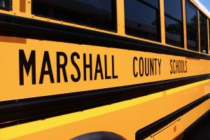 side view of a yellow school bus with Marshall County Schools written in black on the side with black stripes.