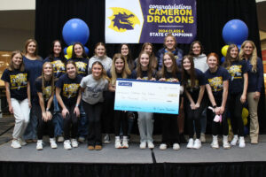 Group picture of the Cameron High School girls’ basketball team on a stage at the mall with a large check.