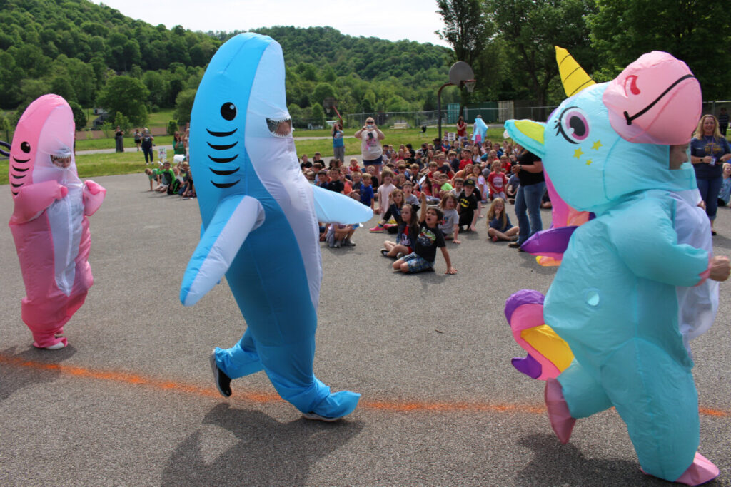 Two inflatable sharks and an inflatable unicorn race on the playground. 