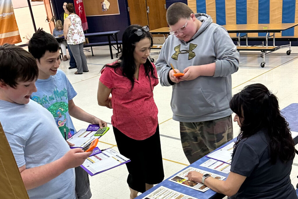 Pictured from left: GAC middle school students David Dove, Aiden Trotto and RJ Beck are assisted by GAC teacher Stacy Hooper, center, while they pay utility bills and adjust their bank statements during the role playing program “Get a Life.”